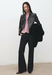 Veste en cuir noire avec deux poches poitrine, pull rose, pantalon noir évasé, et étole en fourrure noire. Des talons aiguilles complètent le look.