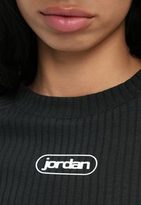 Gros plan sur les lèvres et le menton d'une personne portant un t-shirt noir côtelé avec un logo "jordan" blanc sur la poitrine.