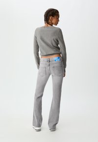 Grå flare-jeans med ett blått varumärkesmidjeband, kombinerat med en åtsittande grå tröja. Tyget verkar mjukt, med en slät textur.