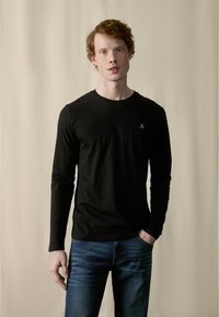 Sort langærmet t-shirt lavet af blødt stof med rund halsudskæring og lille logo på brystet, parret med blå denim jeans.
