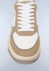 Vita och beige sneaker i mocka och läder, med rund tå, vita snörningar och subtila sömnadsdetaljer.