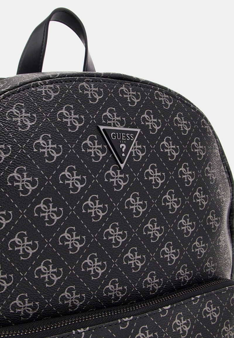 Mochila negra texturizada con un patrón geométrico en gris y una placa central con el logotipo "GUESS" en un triángulo. Cierre con cremallera en la parte inferior.