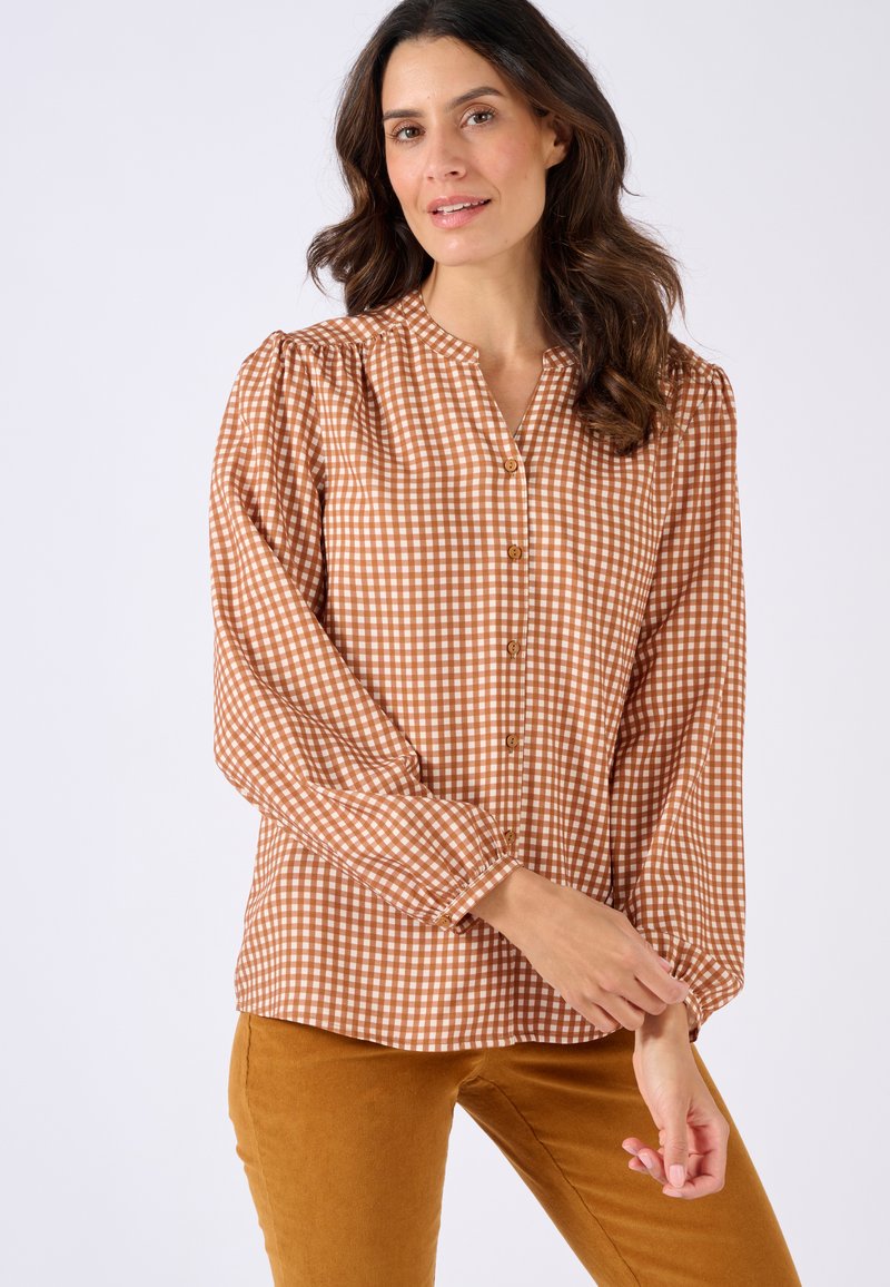 Blusa a scacchi marrone e crema con chiusura a bottoni, maniche a sbuffo e collo arricciato. Abbinata a pantaloni color senape. Tessuto dalla texture liscia.