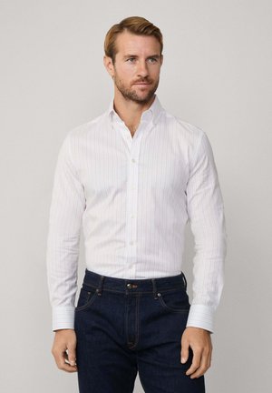 Weißes Hemd mit schmalen rosa Streifen, langen Ärmeln und Kragen, kombiniert mit dunkelblauen Jeans. Glatte Textur und schlanker Schnitt.