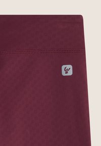 Tessuto sportivo color borgogna con un motivo testurizzato. Un piccolo logo grigio si trova nella parte inferiore. Dettagli delle cuciture visibili sul bordo.