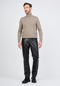 Beige Rollkragenpullover kombiniert mit schwarzen Lederhosen. Der Pullover hat eine taillierte Passform; die Hosen sind elegant und maßgeschneidert, mit einer glatten Textur.