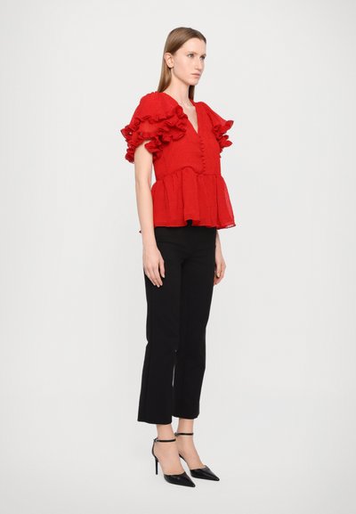 Red textured blouse with ruffled sleeves, button front, and peplum hem paired with black fitted pants and black pointed-toe heels.