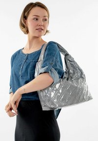 Bolso de mano plateado acolchado con un acabado suave y brillante y una sola correa de hombro ancha. El bolso tiene una forma relajada y detalles de costura visibles.