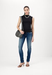 Top negro sin mangas, jeans ajustados azules, sandalias de tacón marrón, bolsa de hombro gris, modelo con trenzas, collar sencillo de cuentas.