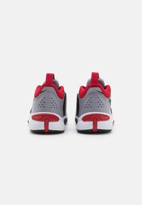 Zapatillas deportivas grises con acentos rojos, que cuentan con una parte superior de malla, detalles perforados y una suela blanca con un patrón de agarre texturizado.