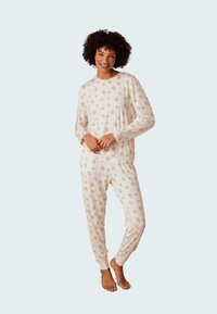 Pitkähihaisista, kevyistä pyjama-setistä, jossa on pehmeä kermaista kangasta ja mansikkakuosi; istuvat hihansuut ja rento malli, jossa on elastinen vyötärö.