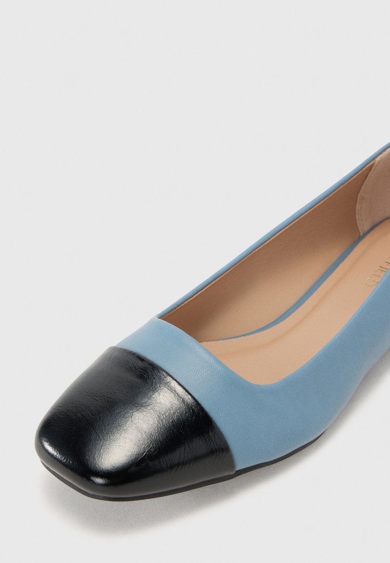 Ballerines en cuir bleu clair avec un embout en cuir verni noir. Texture lisse, forme arrondie avec un petit talon.