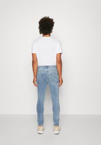 Light blue denim jeans with a slim fit, featuring two back pockets and a smooth texture, paired with a plain white t-shirt.