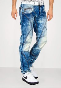 Blauwe denim jeans met vervaagde plekken en diagonale naaddetails. Kenmerkt zich door meerdere zakken, lichter stiksel en een relaxed fit.