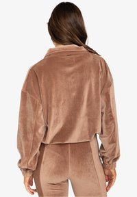 Hnědá oversized kordová bunda s límcem, která má žebrovanou strukturu a elastické manžety. Na zadní straně se nachází jednoduchý detail s visačkou.