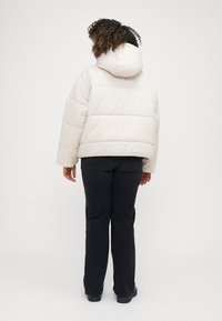 Ανοιχτό μπεζ μαλακό μπουφάν με κουκούλα, με οριζόντια ραφή και χαλαρή εφαρμογή. Συνδυάζεται με μαύρα παντελόνια και παπούτσια.