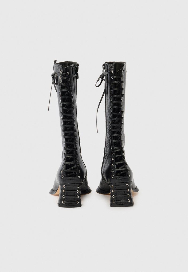 Schwarze kniehohe Stiefel aus Leder mit aufwendiger vorderer Schnürung, dicken Blockabsätzen und dekorativen Schnürungsakzenten an den Fersenseiten.