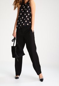 Top senza maniche nero con pois bianchi, abbinato a pantaloni neri larghi e una borsa nera. Le calzature presentano un design bicolore.