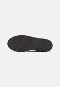 Suela de zapato de goma negra con patrón de agarre, que presenta un detalle de logotipo. La textura suave y los bordes redondeados mejoran la durabilidad y la tracción.