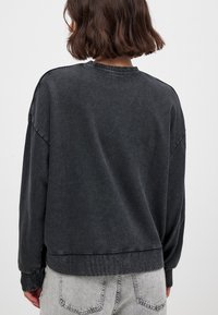 Donkergrijze sweatshirt met een ontspannen pasvorm, geribbelde kraag en manchetten, en een zoom die op de taille valt, met een zachte, gestructureerde stof.
