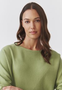 Lys grøn ribbestrikket sweater med et diagonalt teksturmønster, rund halsudskæring og let puffede ærmer. Glat stof, afslappet pasform.