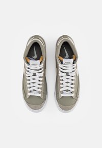 Nike-sneakers i olivgrönt, med en ovandel av canvas, vita snören och gummisula. Utsmyckad med grå och orange detaljer.