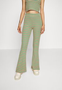 Gestreepte twee-delige outfit in groen, rood en geel; fitted crop top en wijde broek; geribbelde textuur; gecombineerd met chunky witte platform schoenen.
