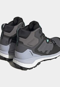 Scarpe da trekking alta in nero e grigio con tomaia in sintetico testurizzato, chiusura con lacci e una suola intermedia bianca e imbottita.