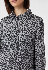 Koszula w czarno-szare w leopardzie cętki z kołnierzykiem, guzikami z przodu i kieszenią na piersi. Wykonana z miękkiego, gładkiego materiału o błyszczącym wykończeniu.