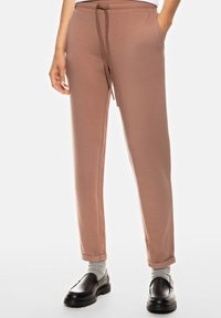 Pantalons de survêtement marron clair avec un cordon de serrage à la taille, coupe fuselée et poignets aux chevilles, associés à des mocassins noirs et des chaussettes grises.