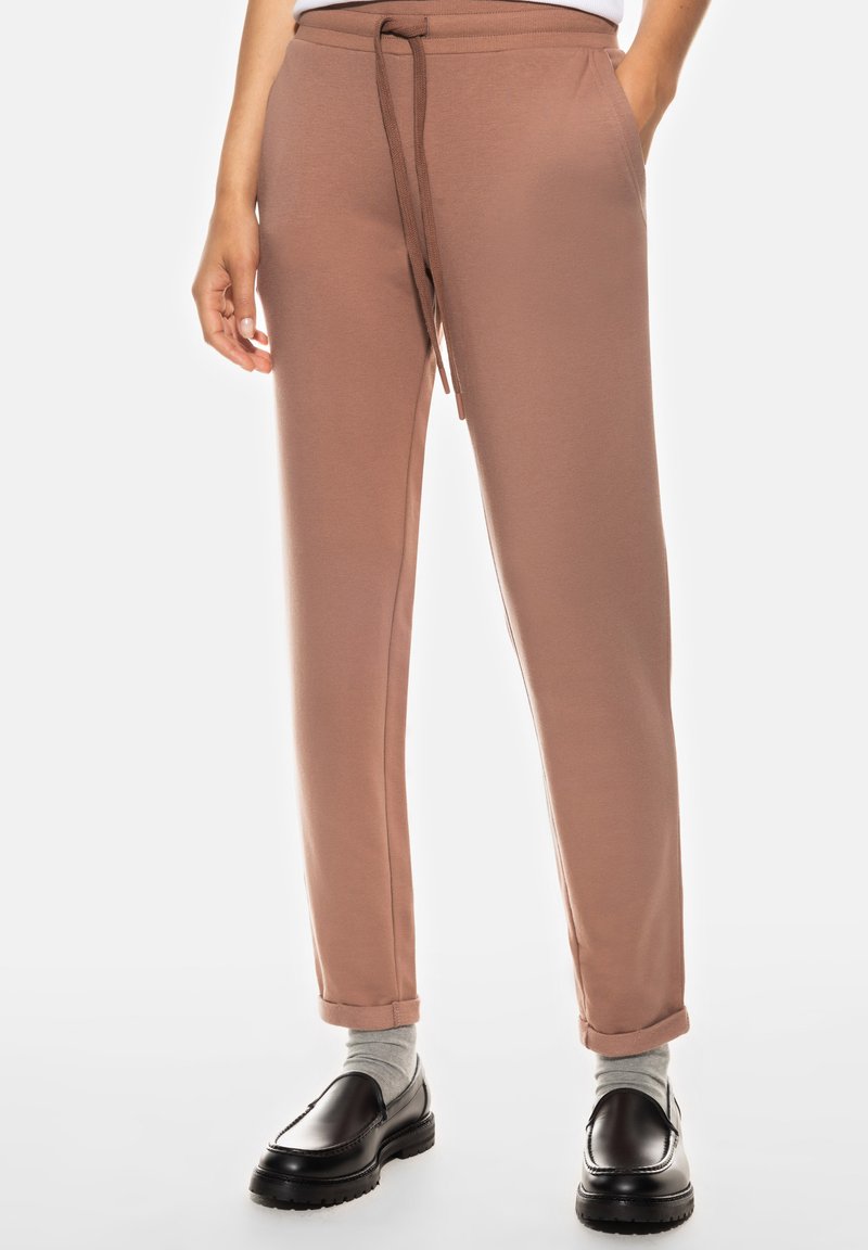 Pantalons de survêtement marron clair avec un cordon de serrage à la taille, coupe fuselée et poignets aux chevilles, associés à des mocassins noirs et des chaussettes grises.