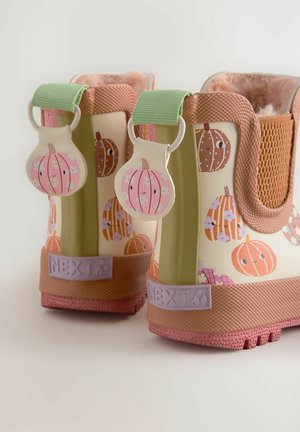 Des bottes de pluie en caoutchouc colorées présentent une base jaune clair avec des motifs de citrouilles et de fleurs, des accents roses, une semelle texturée et des boucles en tissu.