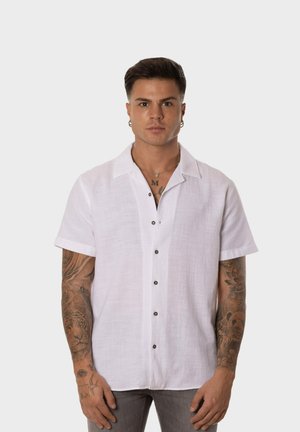 Camisa de manga corta de lino blanco con cuello, que presenta botones marrones en el frente. Tejido texturizado, ajuste relajado, diseño moderno.