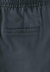 Tissu gris foncé avec une texture lisse, comprenant une taille élastique et une poche arrière cousue. Design simple et fonctionnel.
