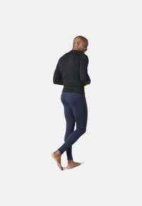 Svart långärmad topp kombinerad med åtsittande marinblå leggings. Materialet verkar vara stretchigt och jämnt. Modellen är barfota och visar en avslappnad hållning.
