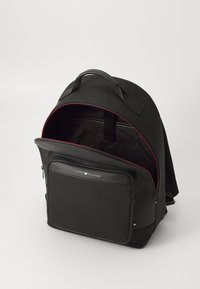Schwarzer Rucksack mit einer glatten Stoffoberfläche und Reißverschlussfächern. Mit roten Akzenten, gepolsterten Trägern und einem auffälligen Logo auf der Vorderseite.