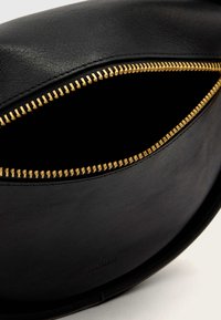 Čierna kožená taška s metalickým zlatým zipsom. Interiér je tmavý a jednoduchý, zdôrazňujúci hladkú textúru a dizajn tašky.