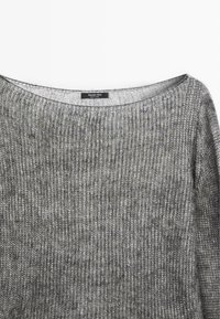 Grå strikket sweater med en bred halsudskæring. Har et struktureret ribbet mønster og et mærke synligt nær kraven. Blødt, let stof.