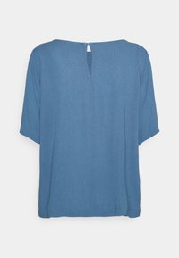 Blouse bleue à manches courtes avec un col rond et un petit détail en forme de trou à l'arrière. Fabriquée dans un tissu léger avec une texture douce.