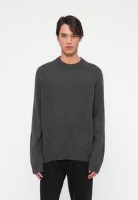 Ciemnoszara dziergana sweter z okrągłym dekoltem, długimi rękawami i ściągaczem na dole. Materiał wydaje się miękki z delikatną teksturą.