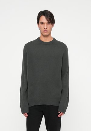 Ciemnoszara dziergana sweter z okrągłym dekoltem, długimi rękawami i ściągaczem na dole. Materiał wydaje się miękki z delikatną teksturą.