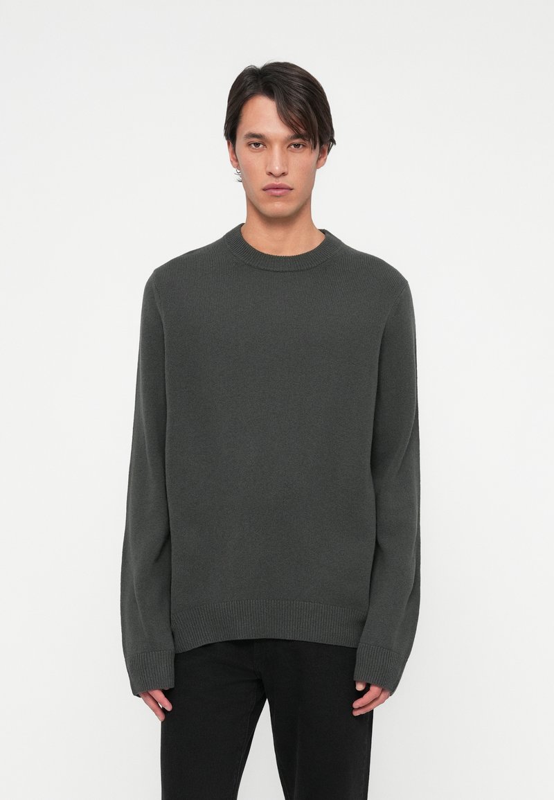 Ciemnoszara dziergana sweter z okrągłym dekoltem, długimi rękawami i ściągaczem na dole. Materiał wydaje się miękki z delikatną teksturą.