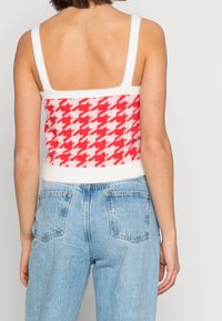 Červený a bílý svetr s rybí kostí, širokými ramínky a chlupatým vzhledem, doplněný světle modrými džíny s vysokým pasem a kapsami.