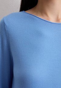 Hellblauer Pullover mit einer glatten Textur, rundem Ausschnitt und dezentem Nähedetail entlang des Ausschnitts und der Schulternaht.
