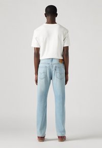 Ljust blå denimjeans med rak bendesign, som har en brun läderpatch och röd sömnad på bakfickorna. Vit t-shirt ovanför.