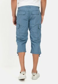 Light blue cargo shorts with side pockets and adjustable hems, made of lightweight fabric, pairing with white sneakers.