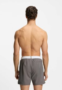 Grijze zwembroek met een elastische witte tailleband en een achterzak. De stof oogt licht en glad.