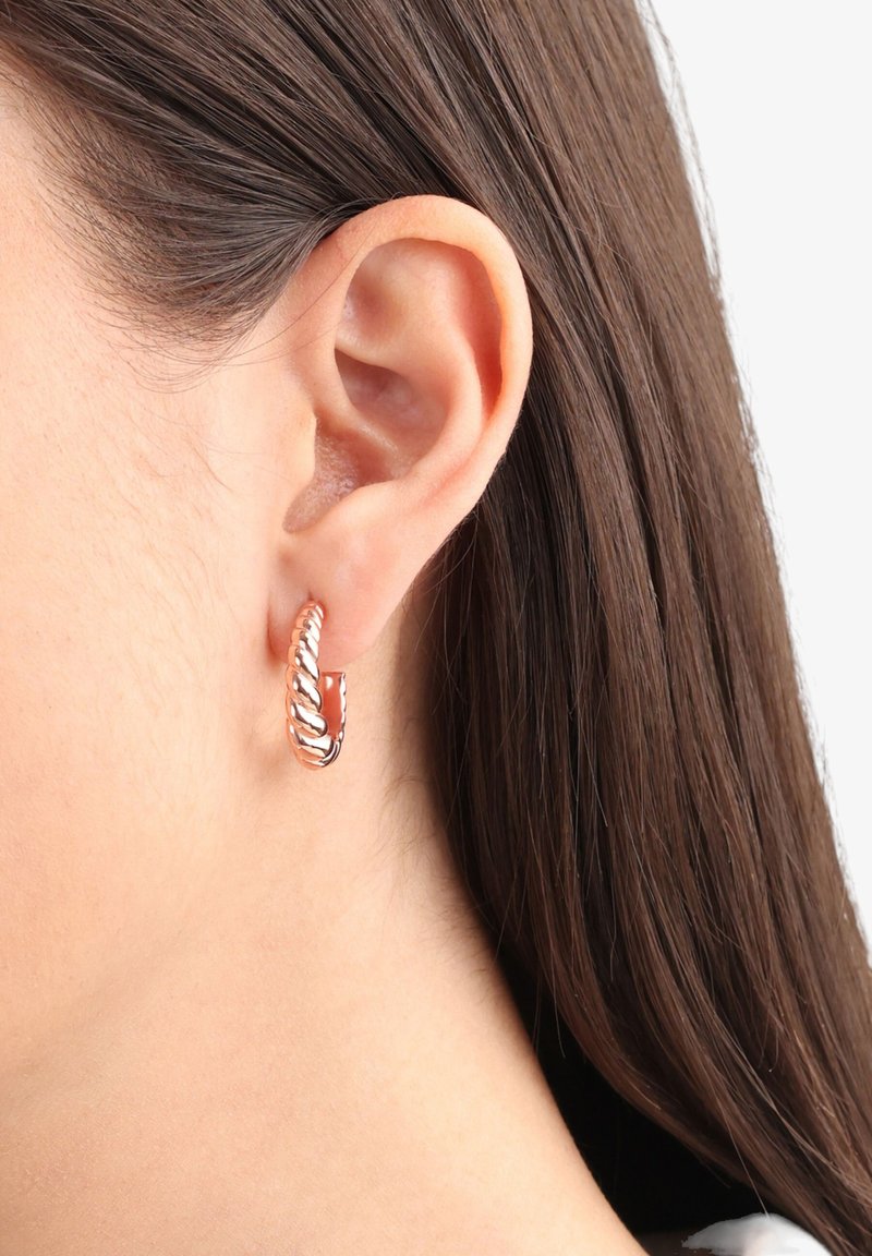 Pendientes de aro en oro rosa con un diseño de cuerda retorcida, que cuentan con un acabado suave y una textura pulida, llevados en una oreja perforada.