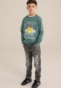Groene trui met een Spongebob-graphic, gecombineerd met grijze jeans en zwarte sneakers. Casual pasvorm, ribgebreide boorden en een ronde halslijn.