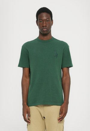 T-shirt en coton vert avec un col rond et des manches courtes. Présente un logo subtil en vert foncé sur la poitrine. Texture lisse.
